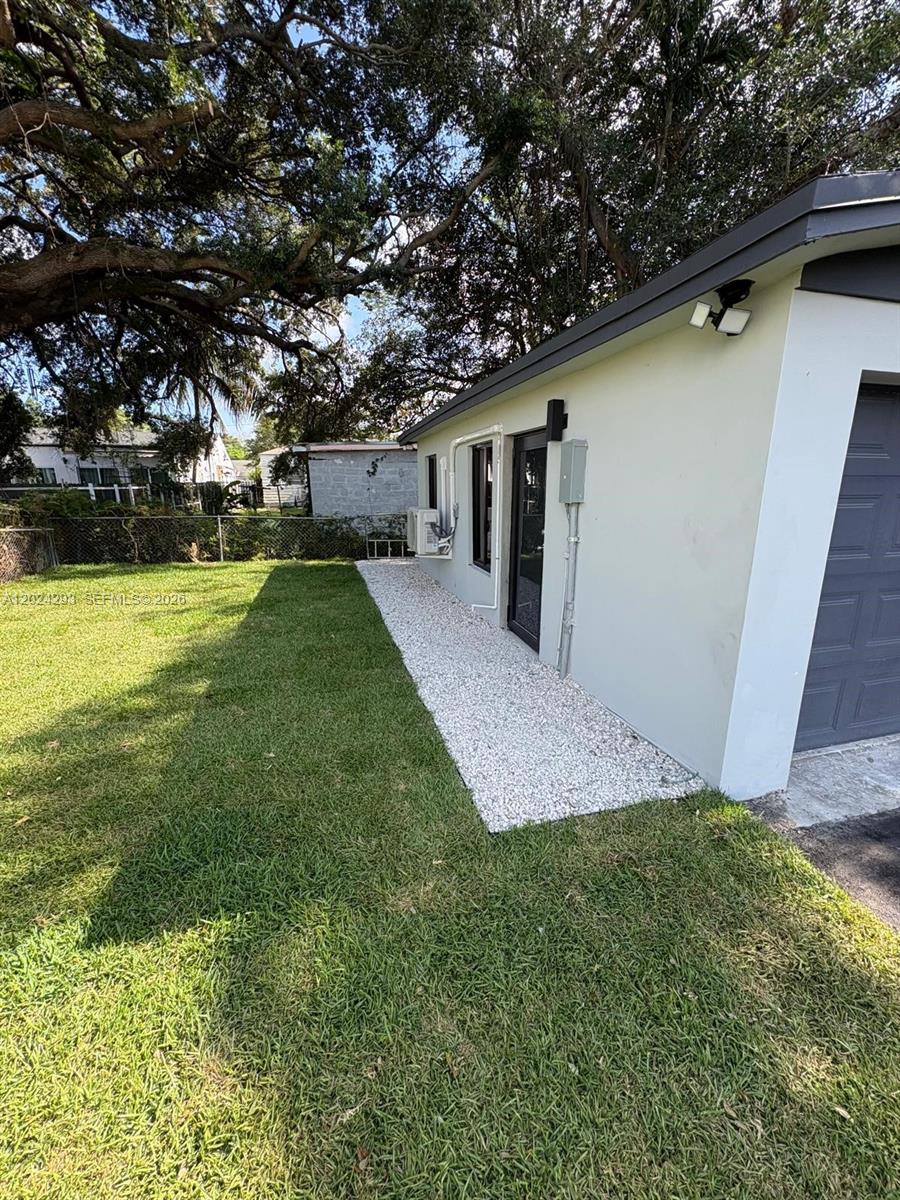 A side view of a house exterior featuring a gravel path, lawn, and large tree — MIAMI, FL