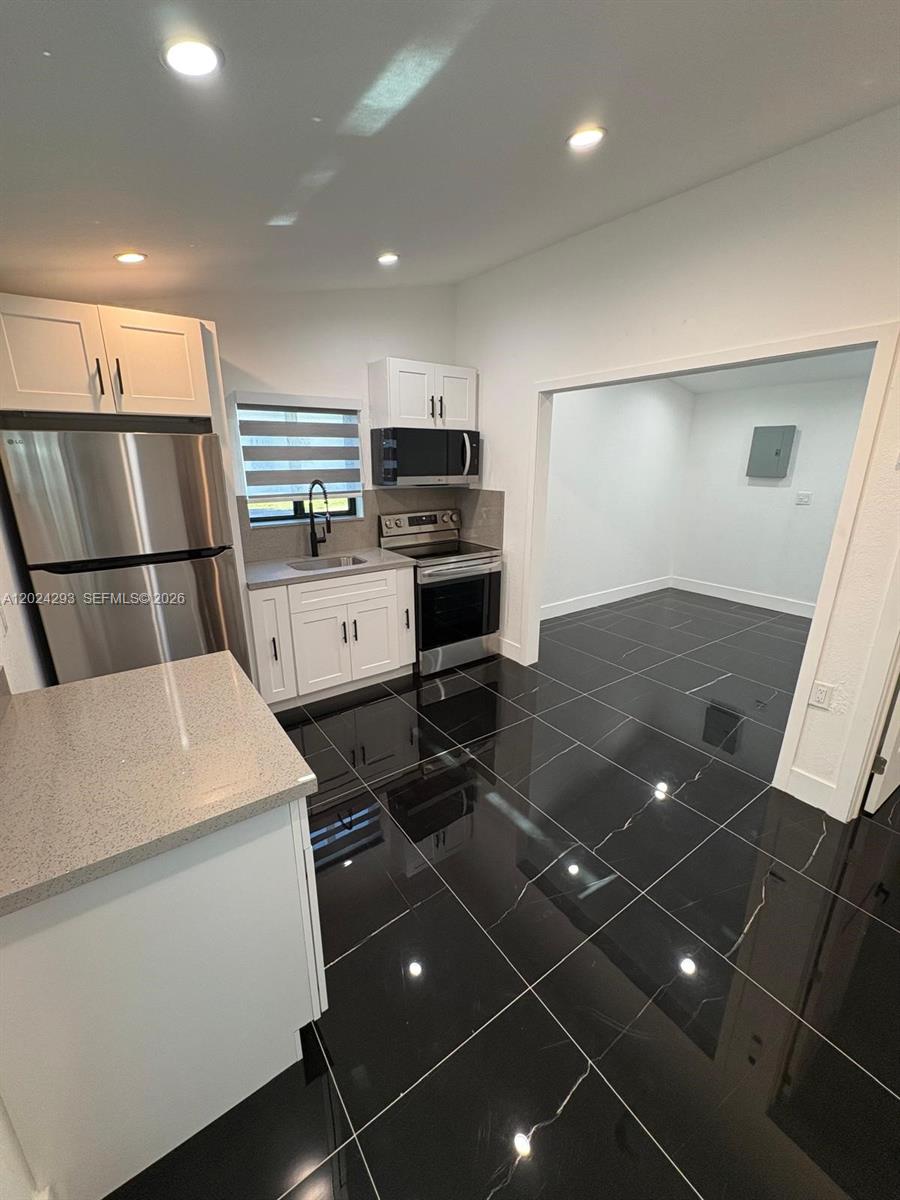 A kitchen features white cabinets, stainless steel appliances, and black tiled flooring — MIAMI, FL