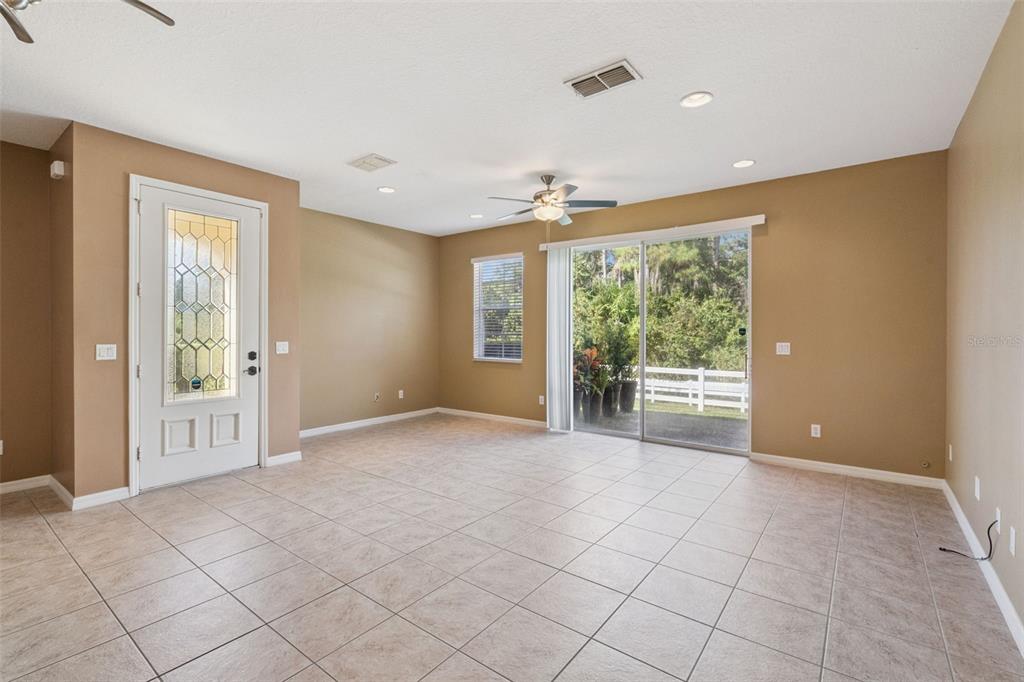 An empty living room features tan walls, tile flooring, a ceiling fan, and sliding doors — 10376 FALLSGROVE STREET, ORLANDO, FL