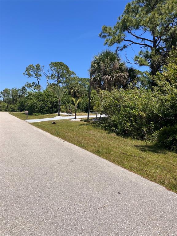 A paved road leads to a vacant, tree-lined lot with a small concrete driveway entrance — 6146 TEDDER STREET, PORT CHARLOTTE, FL