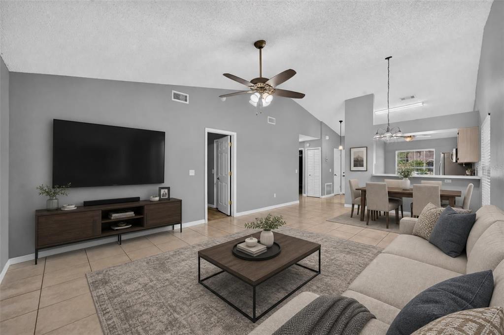 A living room with a vaulted ceiling, tile floors, a large television, and dining area — 117 SHADY OAK LANE, OVIEDO, FL