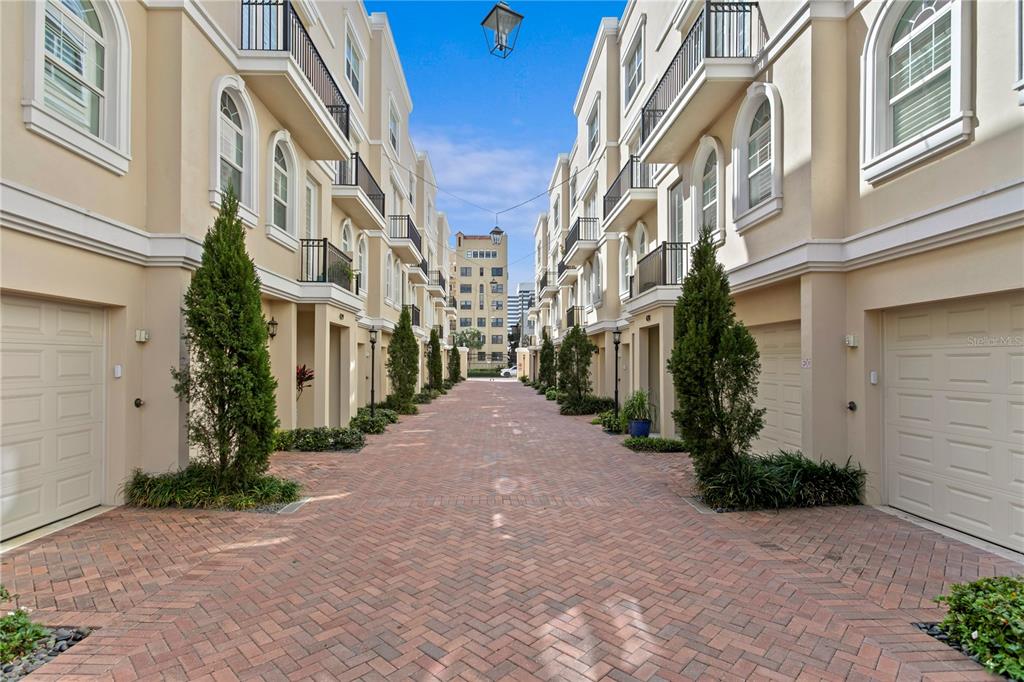 A brick-paved alleyway is flanked by two rows of multi-story townhomes with attached garages — 412 REGENT LANE N, ST PETERSBURG, FL