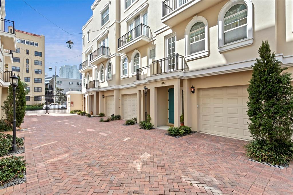 A row of townhouses with beige stucco facades, arched windows, and brick-paved driveways — 412 REGENT LANE N, ST PETERSBURG, FL