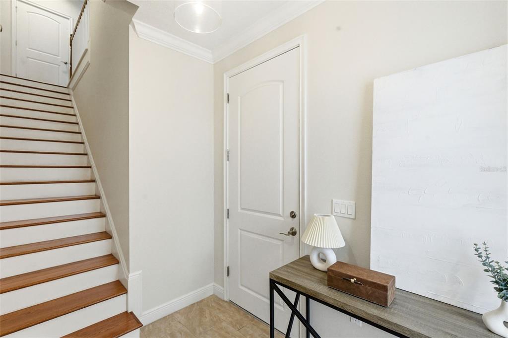 A staircase with wooden treads leads upward next to a white door and console table — 412 REGENT LANE N, ST PETERSBURG, FL