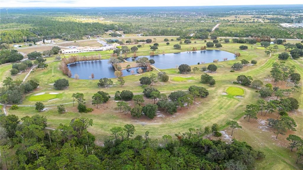 An aerial view of a golf course featuring a large pond and surrounding wooded landscape — 0 OLEANDER DRIVE, INDIAN LAKE ESTATES, FL
