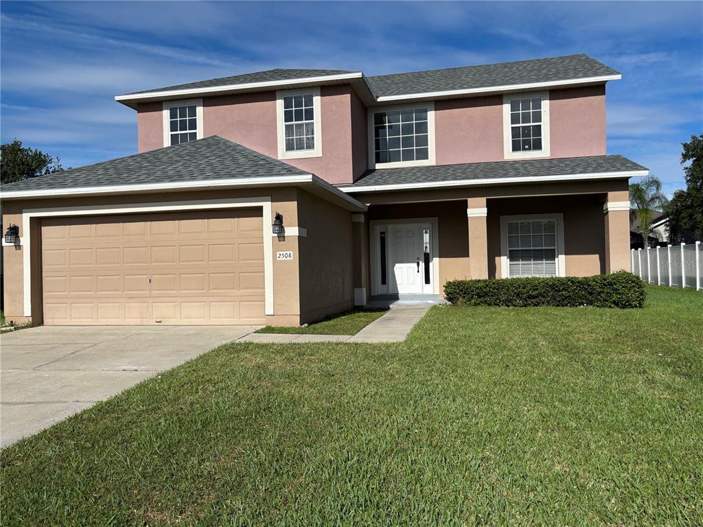 A two-story house with a tan stucco exterior, a two-car garage, and a front porch — 2508 BAYKAL DRIVE, KISSIMMEE, FL