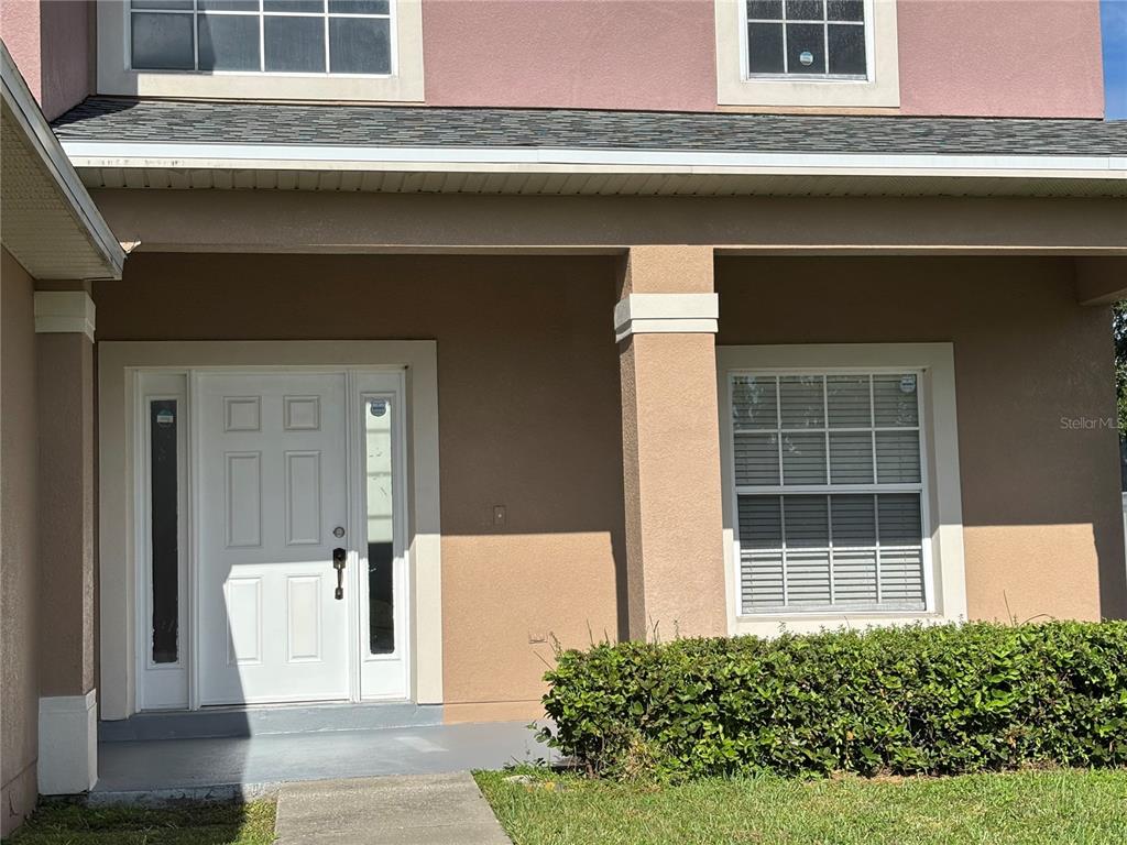 The exterior of a house features a covered entryway, a white front door, and a window — 2508 BAYKAL DRIVE, KISSIMMEE, FL