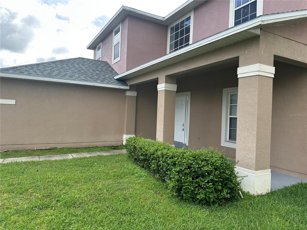 A two-story house with a tan stucco exterior, a covered front porch, and green hedges — 2508 BAYKAL DRIVE, KISSIMMEE, FL