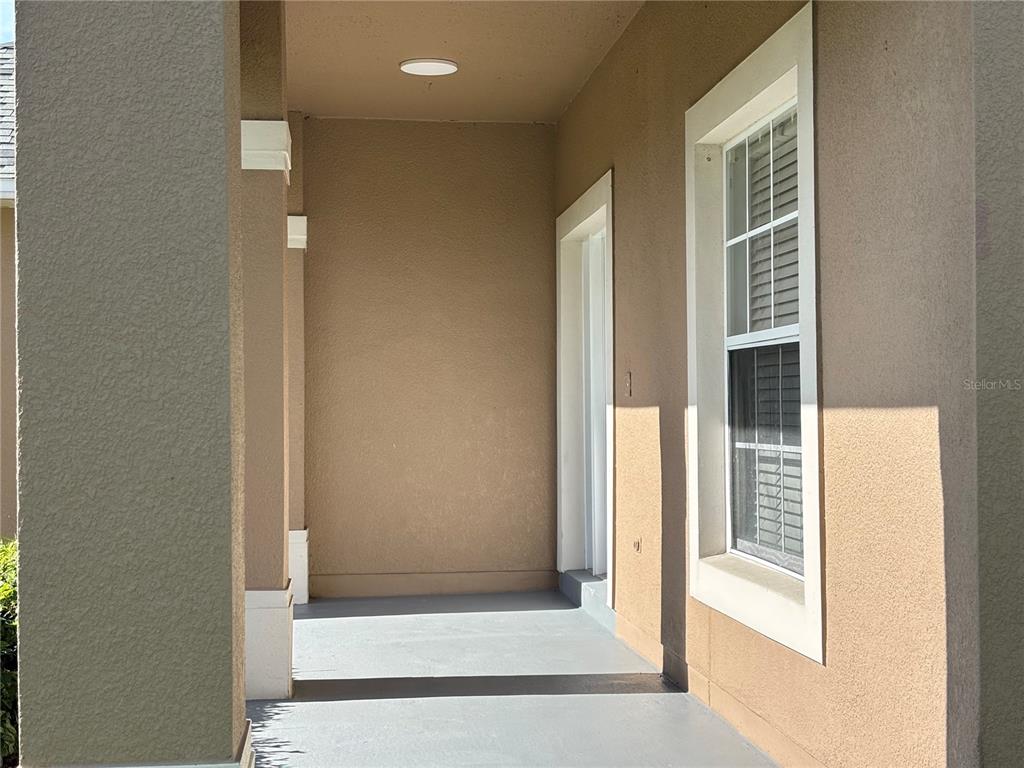 A covered entryway features a gray concrete floor, a beige stucco wall, and a window — 2508 BAYKAL DRIVE, KISSIMMEE, FL
