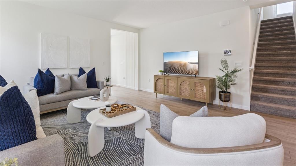 A living room features a grey sofa, white armchairs, a wooden media console, and stairs — 4958 MARSHELDER STREET, APOPKA, FL