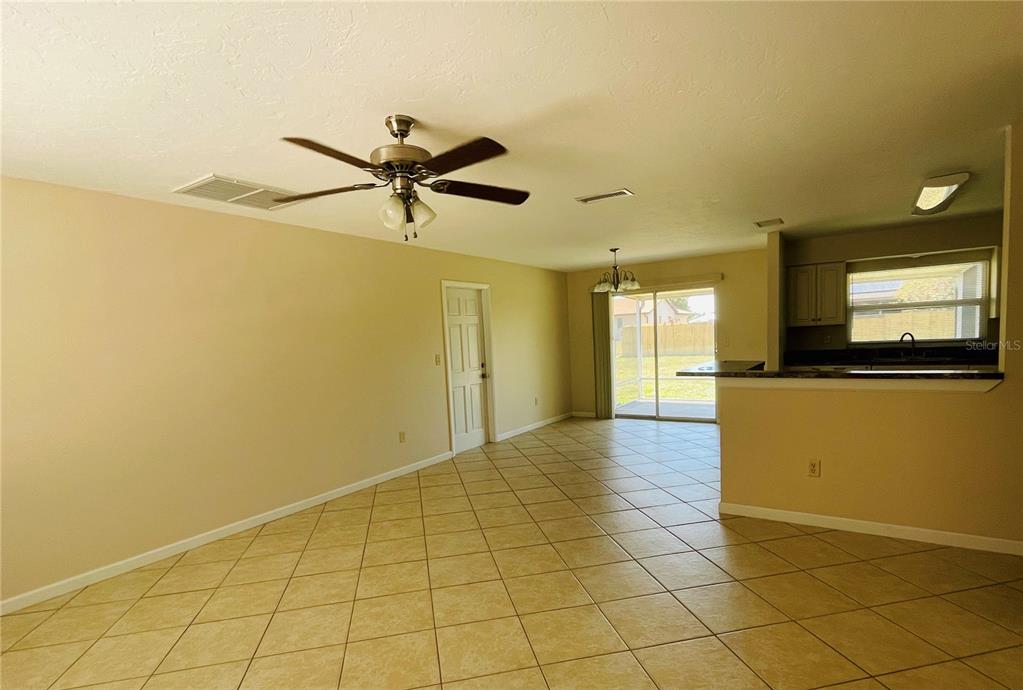An open-concept room features beige walls, tiled floors, a ceiling fan, and a kitchen pass-through — 1506 DEWITT STREET, PORT CHARLOTTE, FL
