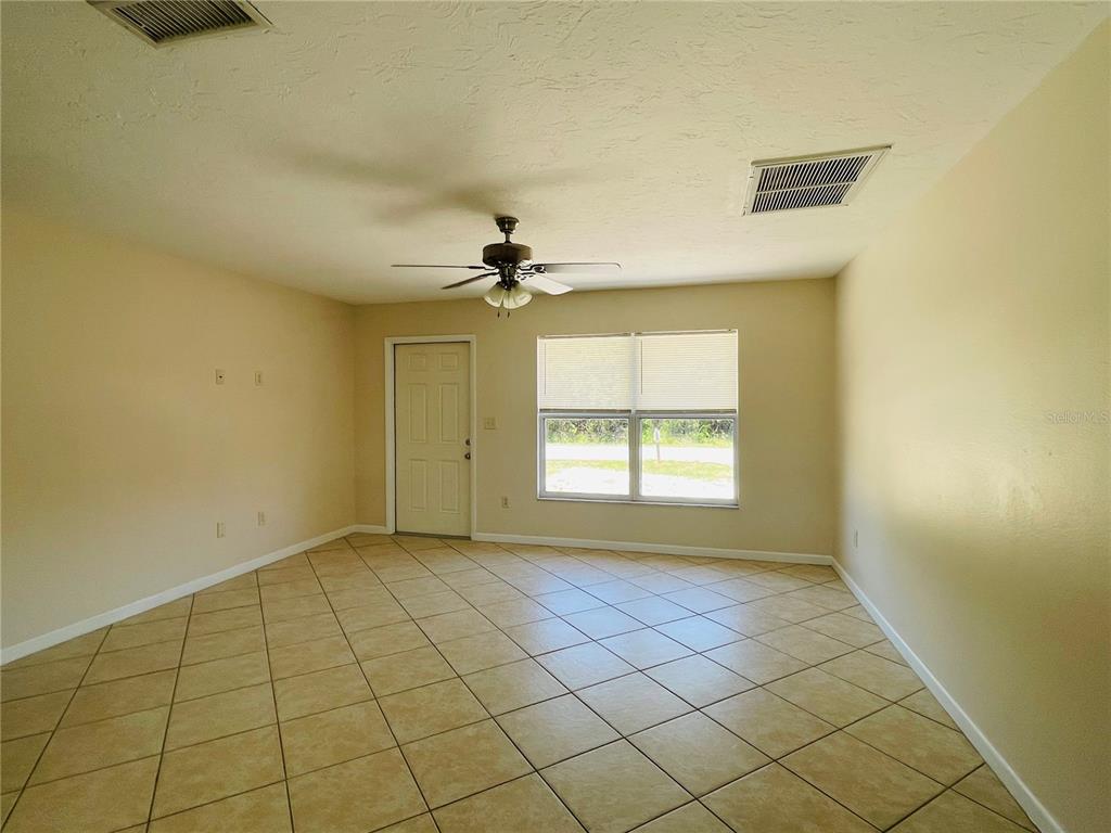 An empty room features beige walls, a tiled floor, a ceiling fan, and a door — 1506 DEWITT STREET, PORT CHARLOTTE, FL