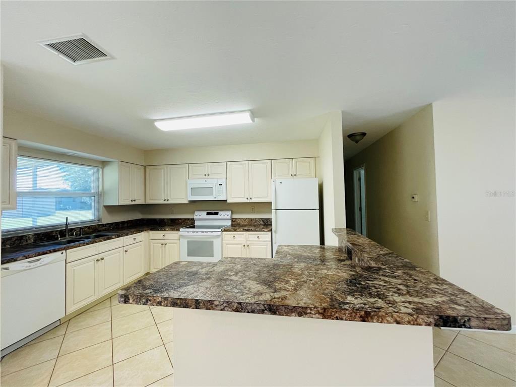 A kitchen features white cabinets, dark granite countertops, white appliances, and light-colored tile flooring — 1506 DEWITT STREET, PORT CHARLOTTE, FL