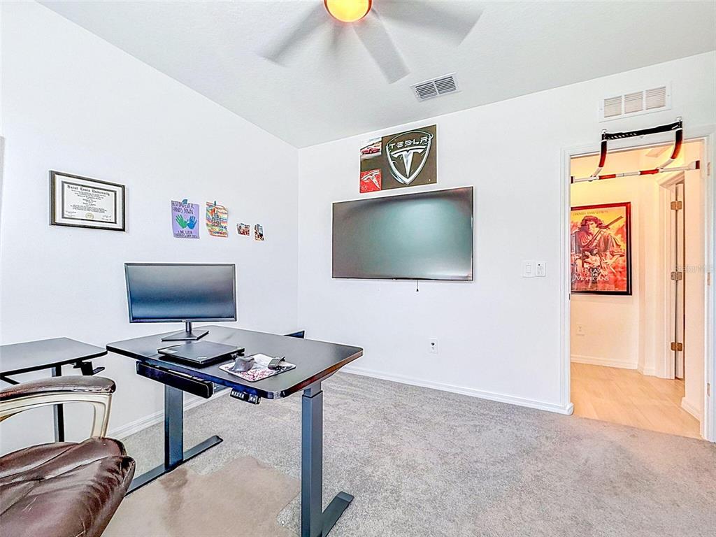 A home office features a standing desk, a wall-mounted television, and a pull-up bar — 12227 RADIANT GEM TRAIL, PARRISH, FL