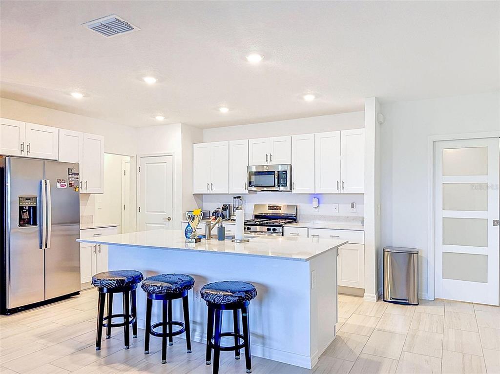A modern kitchen features white cabinetry, a central island with three stools, and stainless appliances — 12227 RADIANT GEM TRAIL, PARRISH, FL