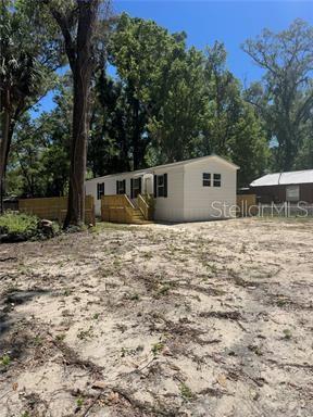 A light-colored mobile home sits on a sandy lot with wooden stairs and a fence — 8630 SW 82ND TERRACE, TRENTON, FL