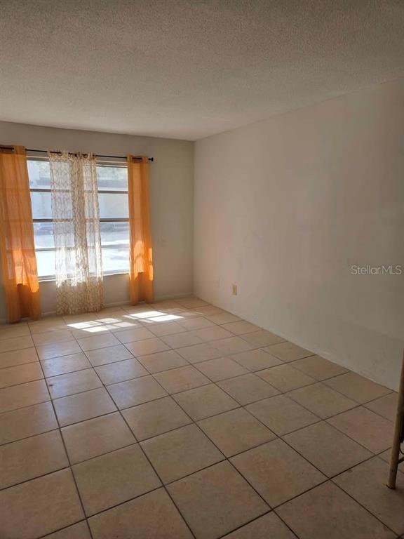 An empty room features light-colored floor tiles, white walls, and windows with orange curtains — 3715 COLBY STREET, SARASOTA, FL