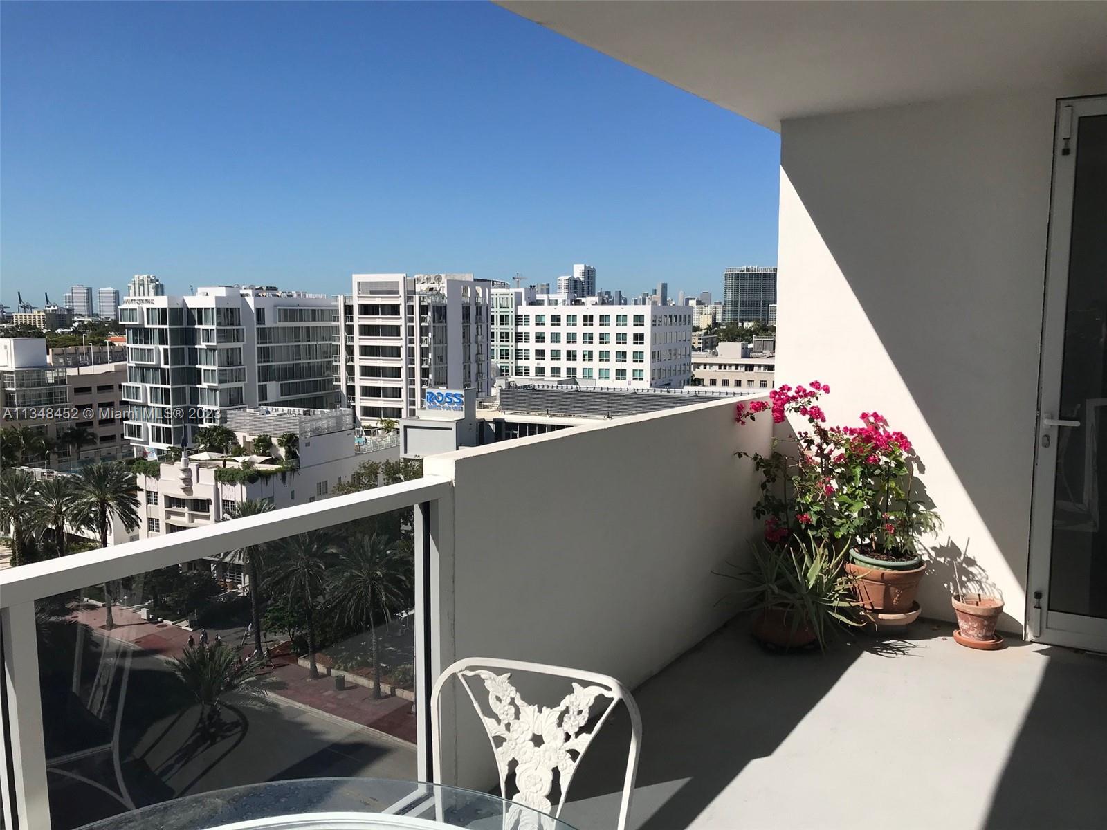 A balcony with a white railing, a metal chair, potted plants, and a city view — 100 Lincoln Rd # 1007, Miami Beach FL 33139, MIAMI BEACH, FL