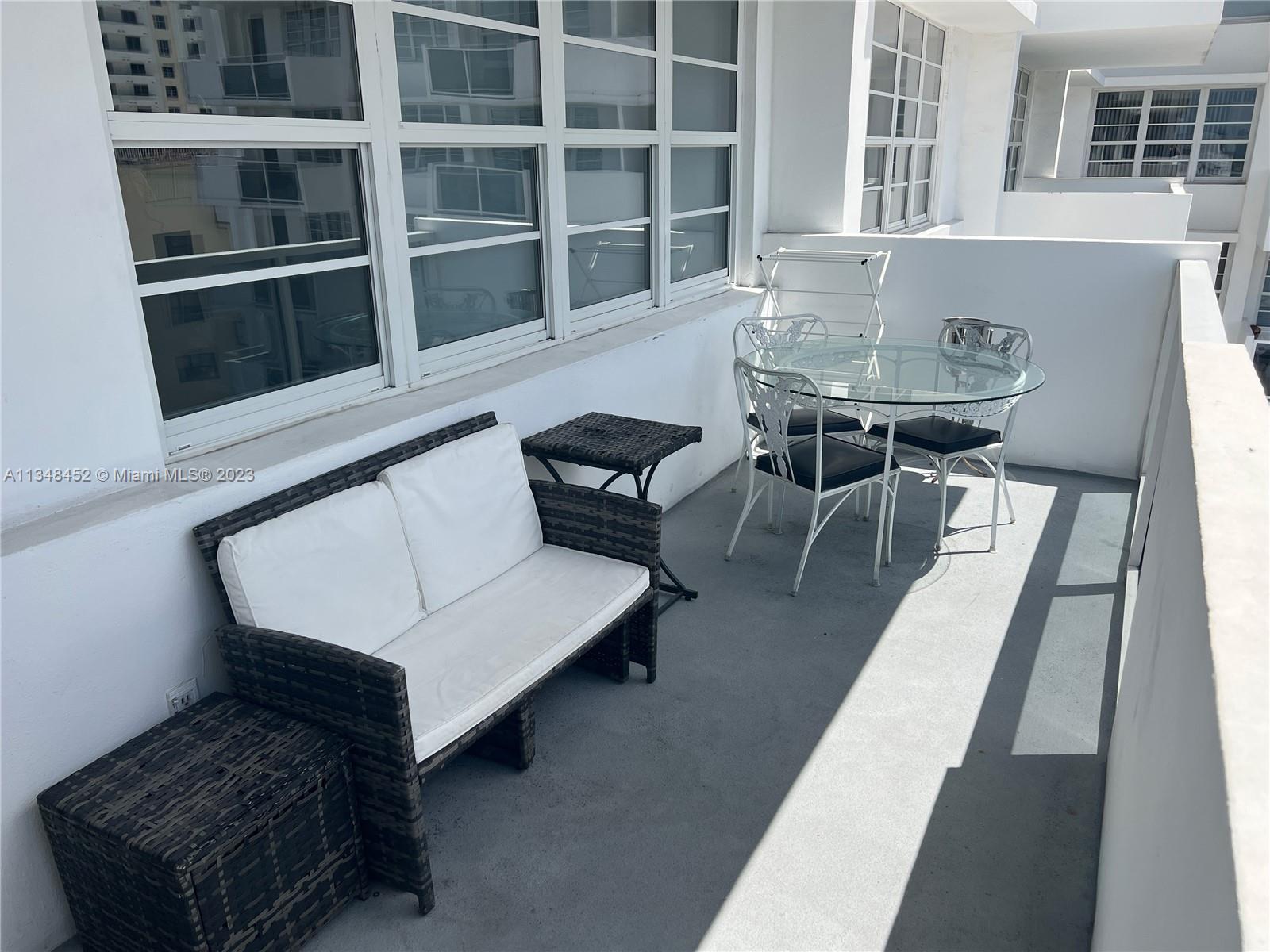 A balcony features a wicker loveseat, a glass-topped dining set, and large windows — 100 Lincoln Rd # 1007, Miami Beach FL 33139, MIAMI BEACH, FL