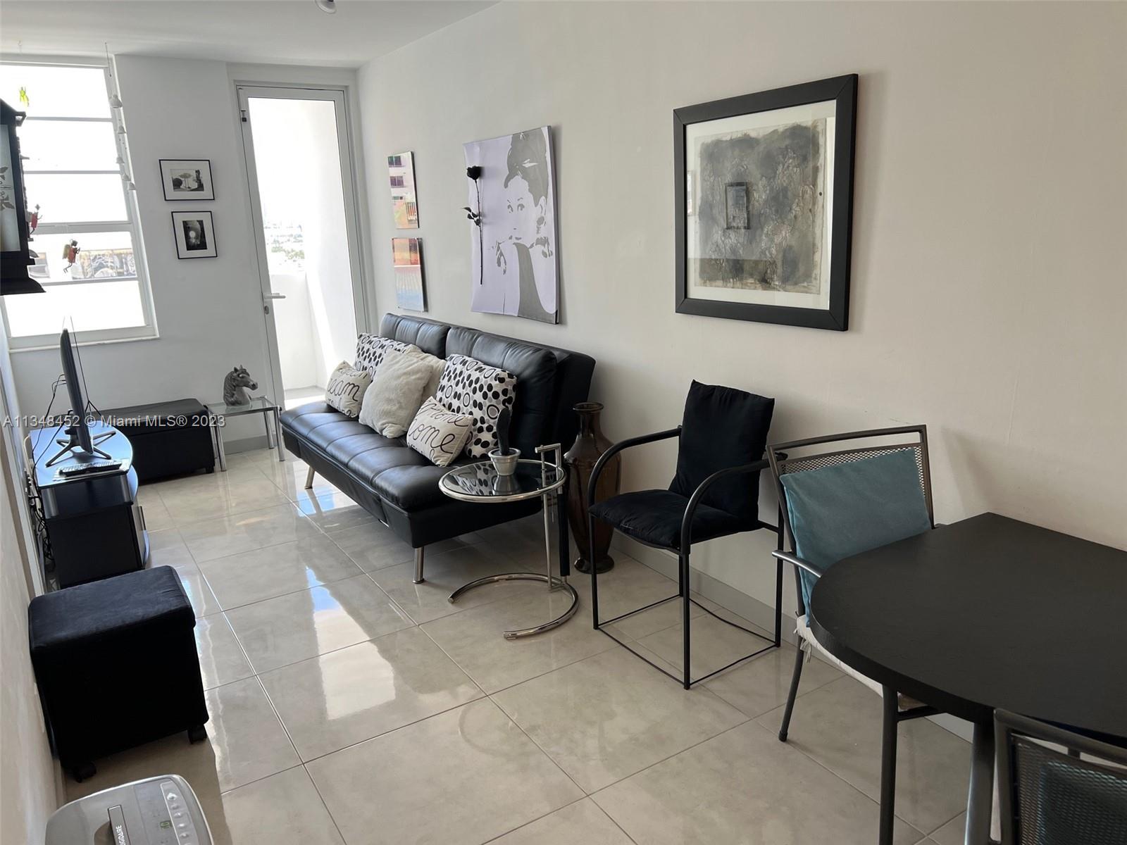 A living room features a black sofa, a dining table, and light-colored tile flooring — 100 Lincoln Rd # 1007, Miami Beach FL 33139, MIAMI BEACH, FL