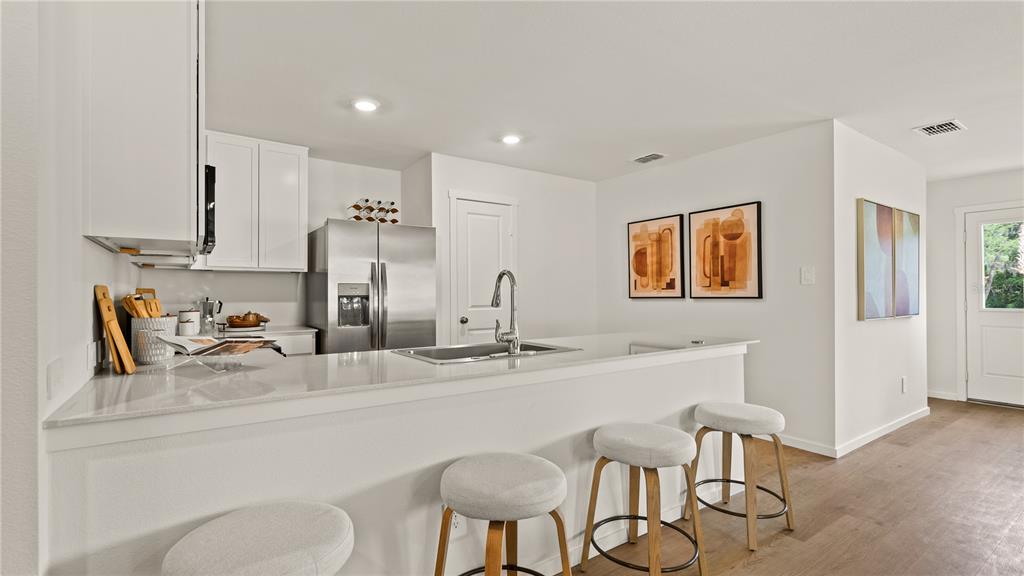 A modern kitchen features white cabinets, stainless steel appliances, a quartz island, and bar stools — 6103 SWAMP BAY DRIVE, EDGEWATER, FL