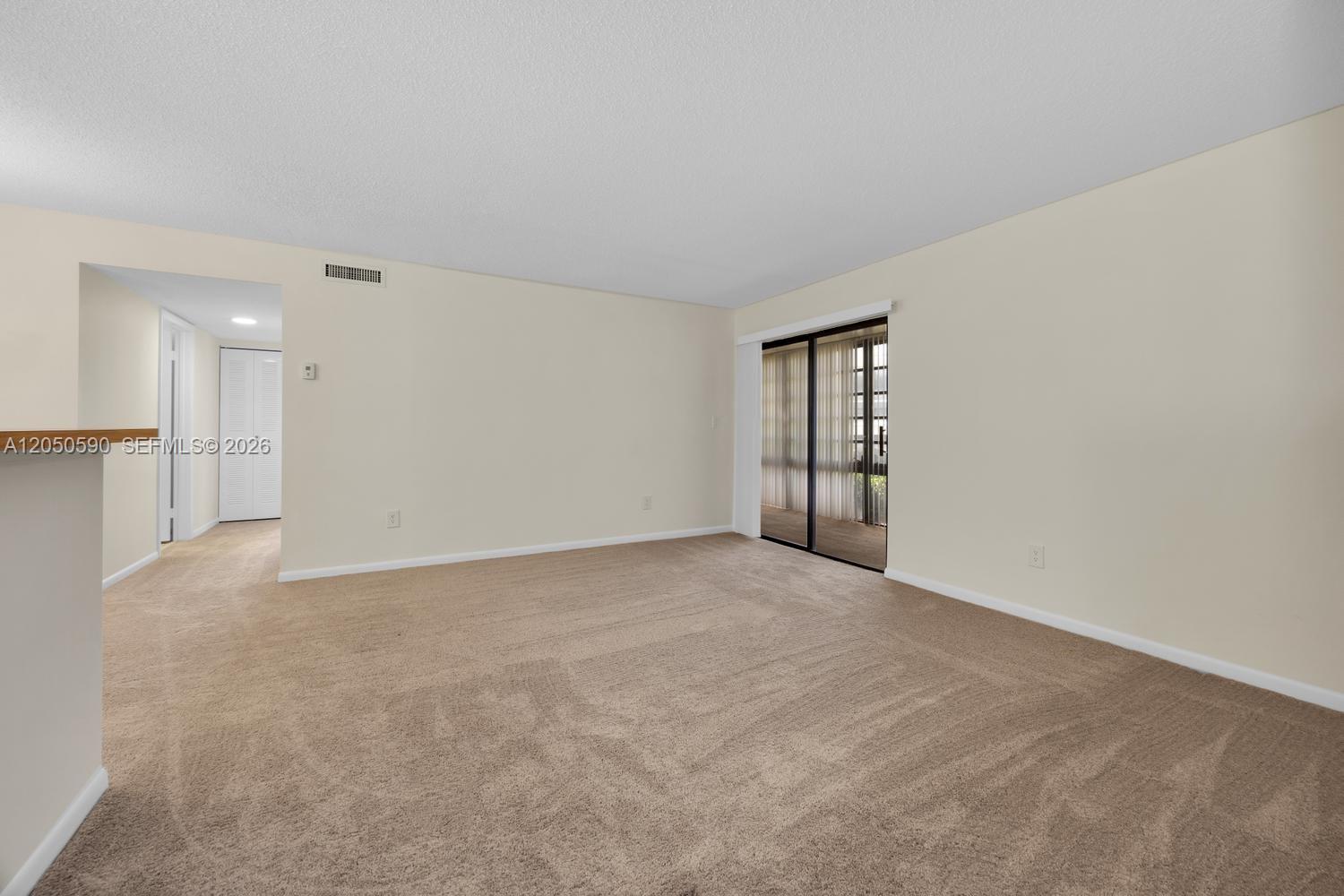An empty living room features beige carpeting, light-colored walls, and a sliding glass door — 9711 Hammocks Blvd # K, Miami FL 33196, MIAMI, FL
