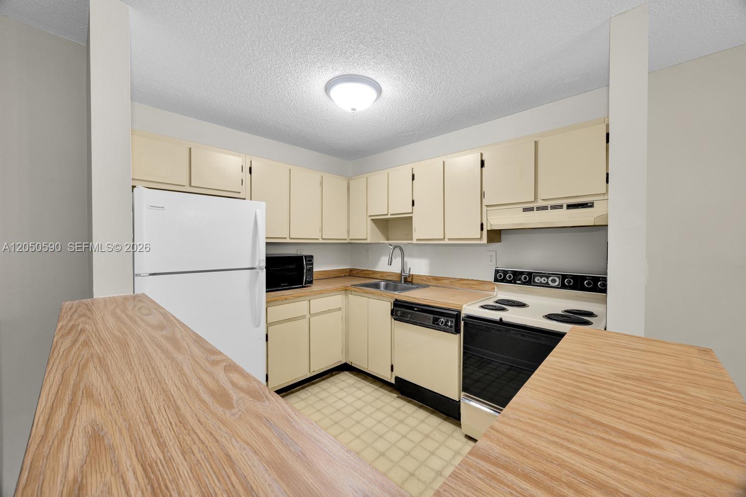 This kitchen features light-colored cabinets, wood-look countertops, and white appliances — 9711 Hammocks Blvd # K, Miami FL 33196, MIAMI, FL