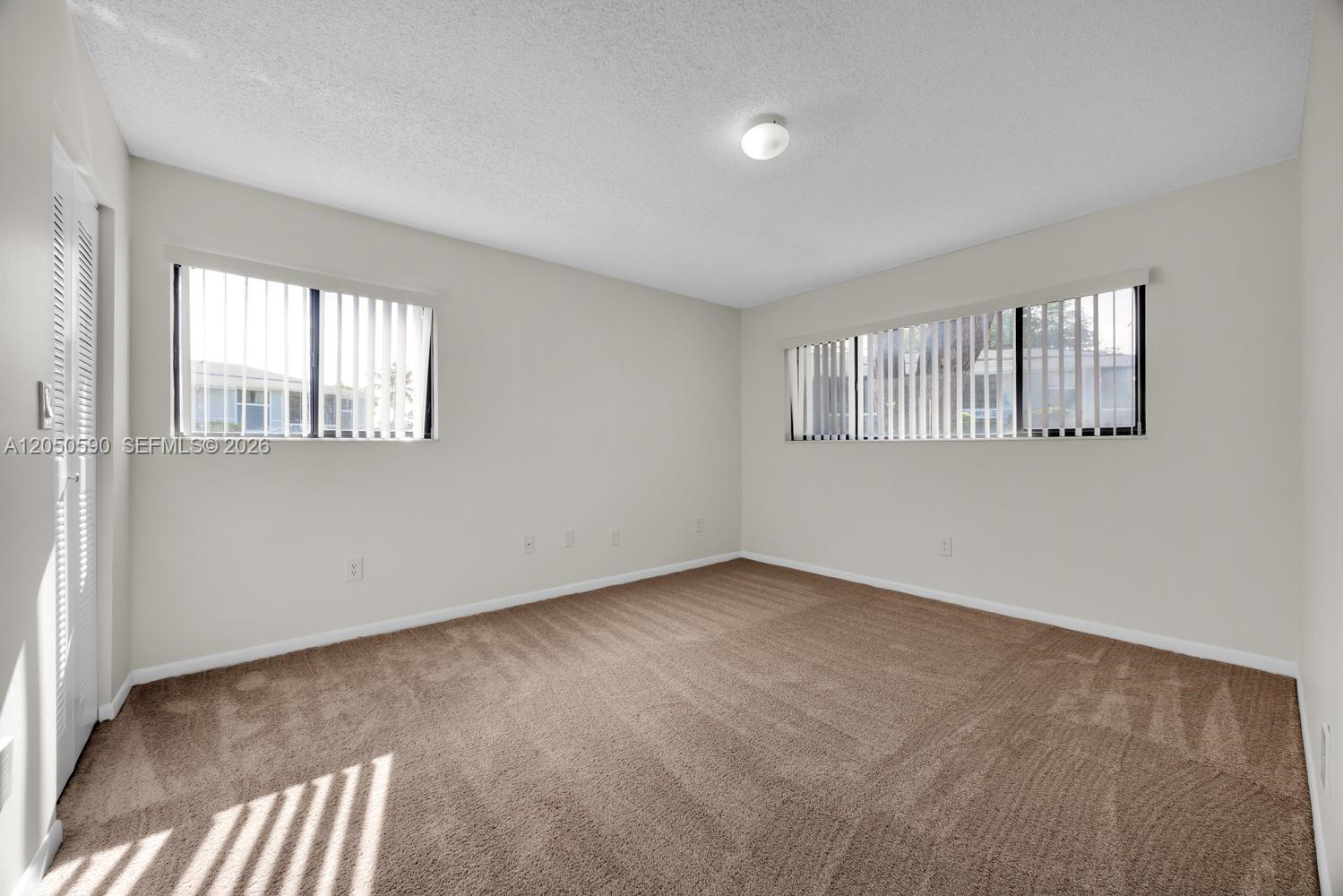 An empty bedroom features beige walls, brown carpeting, and two windows with vertical blinds — 9711 Hammocks Blvd # K, Miami FL 33196, MIAMI, FL