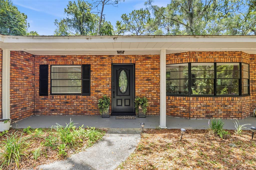 A brick house exterior features a black front door, a covered porch, and large windows — 9661 W DEEPWOODS DRIVE, CRYSTAL RIVER, FL