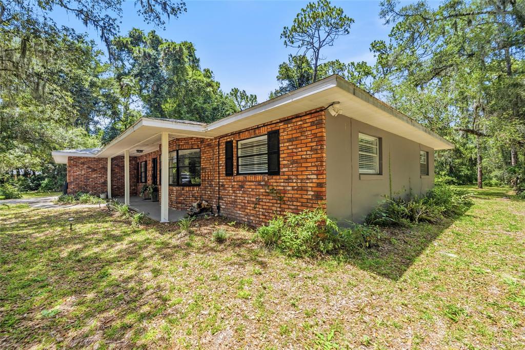 A single-story brick house with a covered porch sits on a grassy, tree-filled lot — 9661 W DEEPWOODS DRIVE, CRYSTAL RIVER, FL