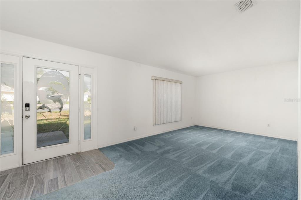 A living room features blue carpeting, white walls, a front door with glass, and vertical blinds — 49 BAHIA TRACE COURSE, OCALA, FL