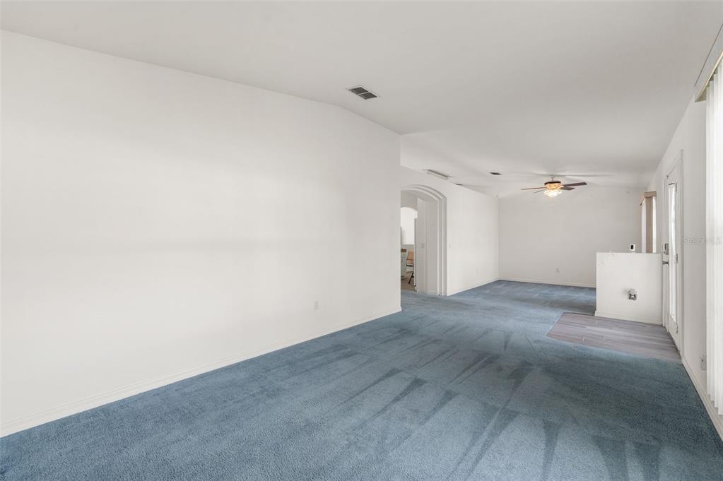 A spacious living area features blue carpeting, white walls, and a ceiling fan — 49 BAHIA TRACE COURSE, OCALA, FL
