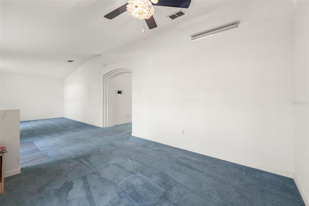 An empty room with blue carpeting, white walls, a ceiling fan, and an arched doorway — 49 BAHIA TRACE COURSE, OCALA, FL