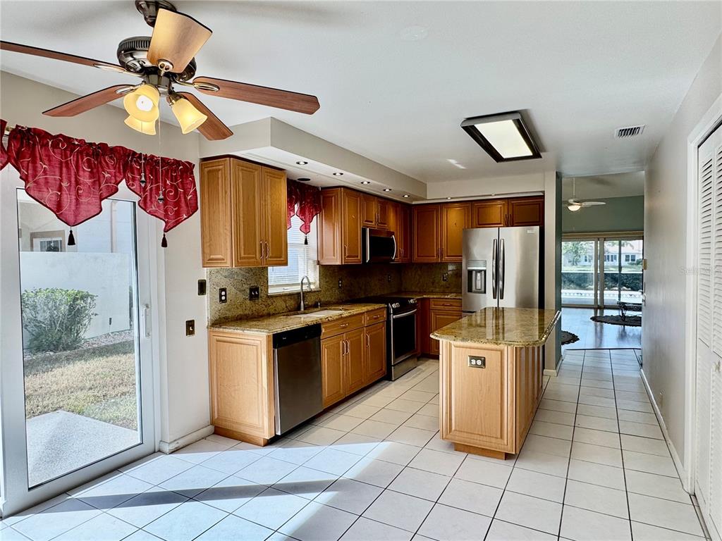 A kitchen features light wood cabinets, granite countertops, stainless steel appliances, and white tile flooring — 4720 PERIDIA BOULEVARD E, BRADENTON, FL
