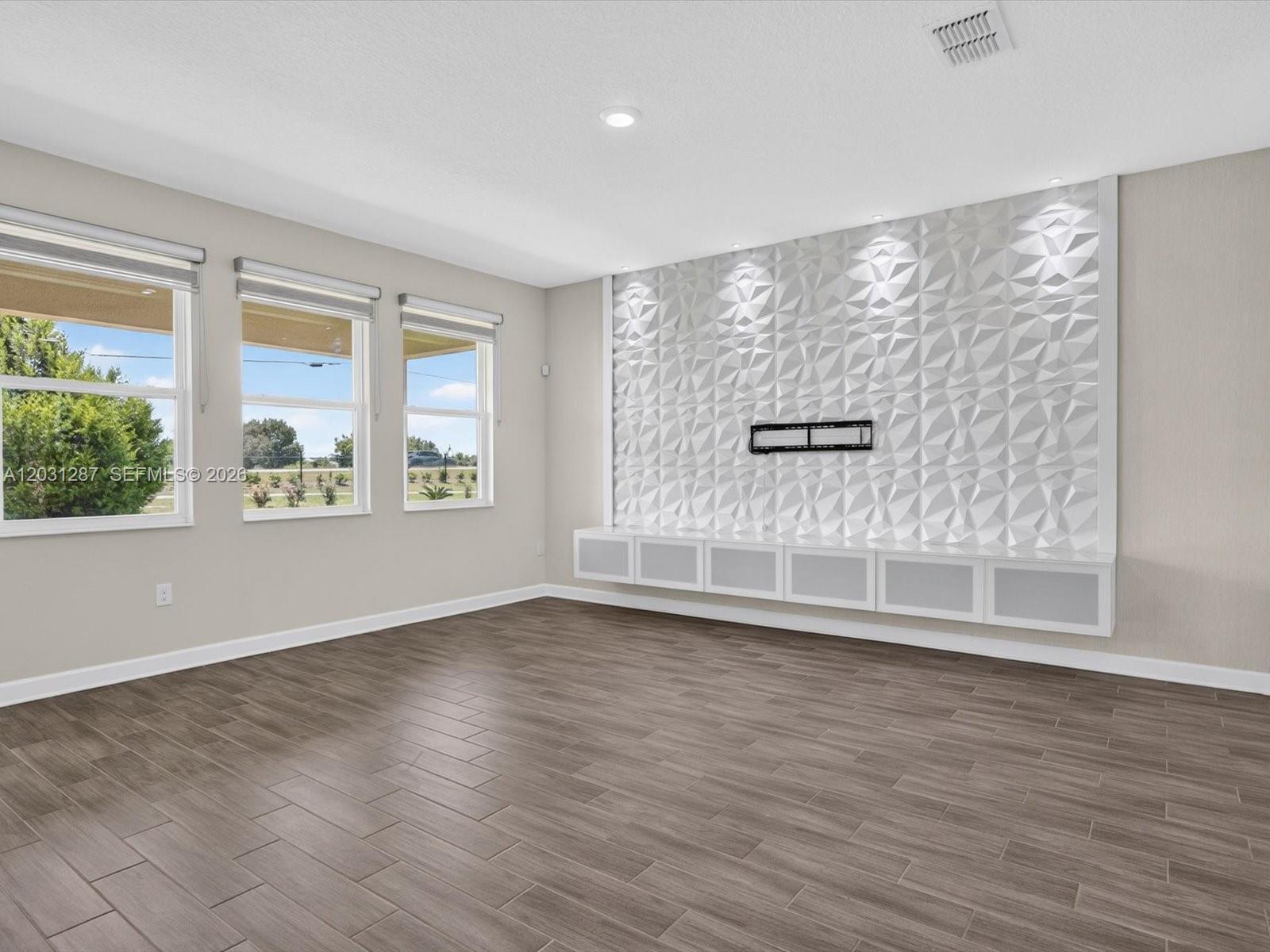 A living room features wood-look tile flooring, three windows, and a textured white accent wall — 1152 Trappers Trail Loop, Davenport FL 33896, DAVENPORT, FL