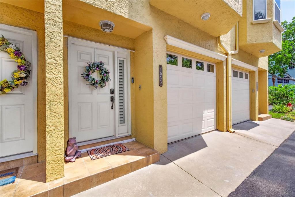 A yellow stucco townhouse exterior features a white front door, a garage, and a wreath — 1033 PINELLAS BAYWAY  S, TIERRA VERDE, FL