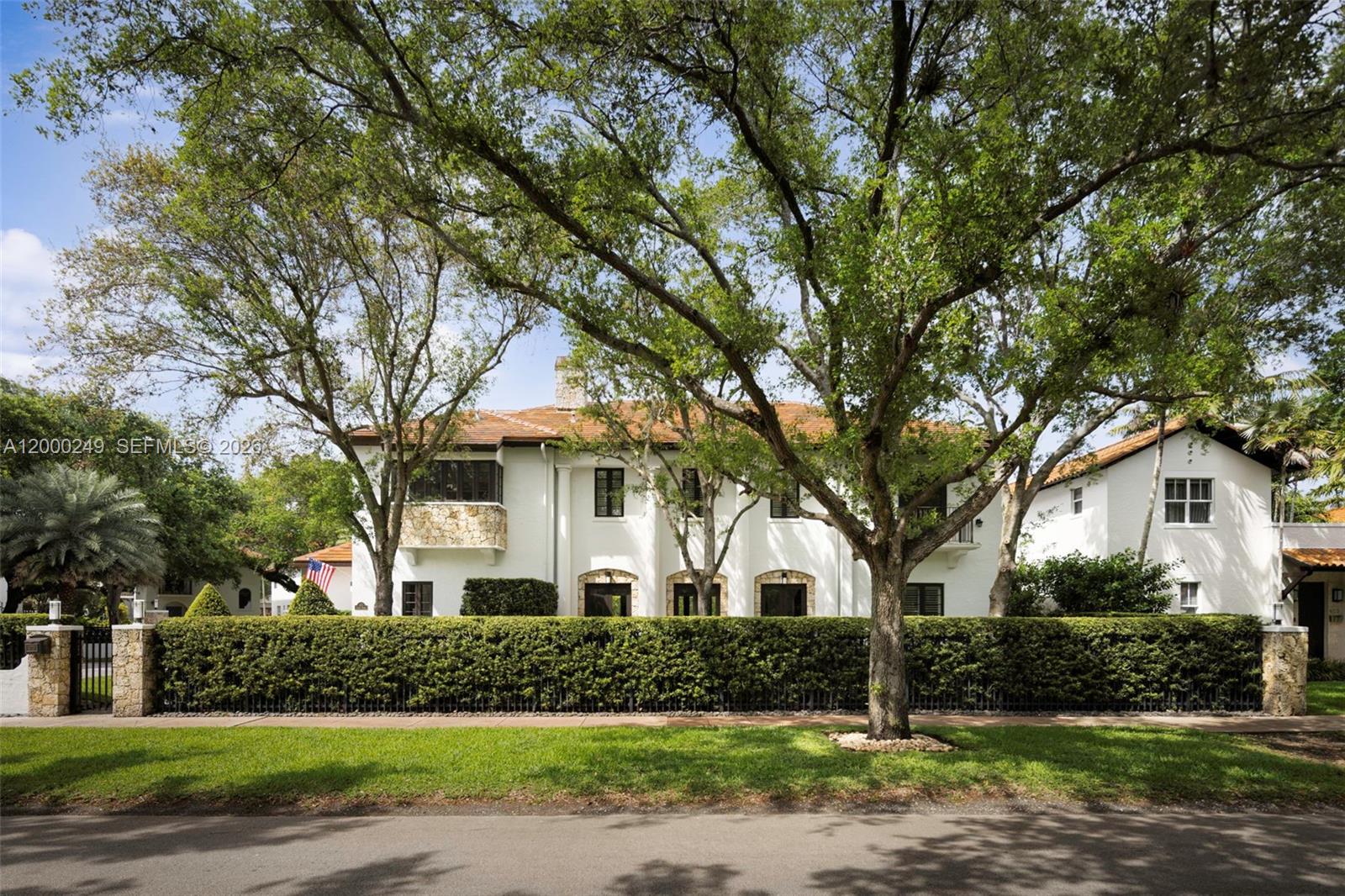 A two-story white stucco house with a tile roof sits behind a tall green hedge — 475 Amalfi Ave, Coral Gables FL 33146, CORAL GABLES, FL