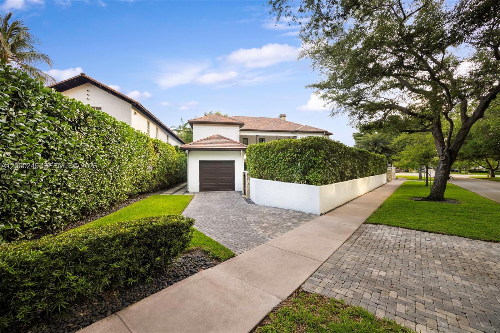 A white house with a brown garage door and a tall hedge-lined driveway — 475 Amalfi Ave, Coral Gables FL 33146, CORAL GABLES, FL