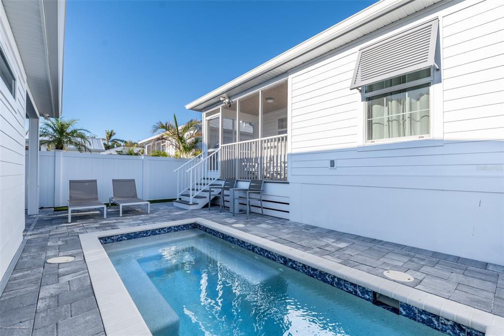 A small rectangular swimming pool sits on a paved patio beside a white house exterior — 327 HARVEY STREET, PUNTA GORDA, FL