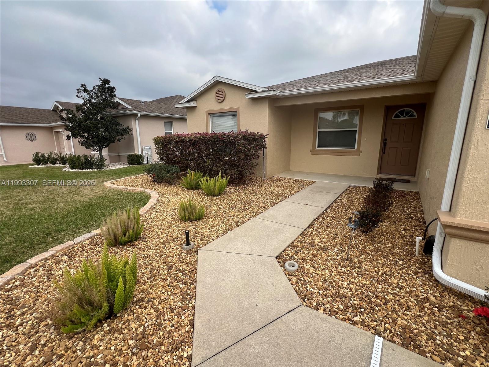A beige house features a concrete walkway leading to the front door and gravel landscaping — 1679 SW 156th Ln, Ocala FL 34473, OCALA, FL