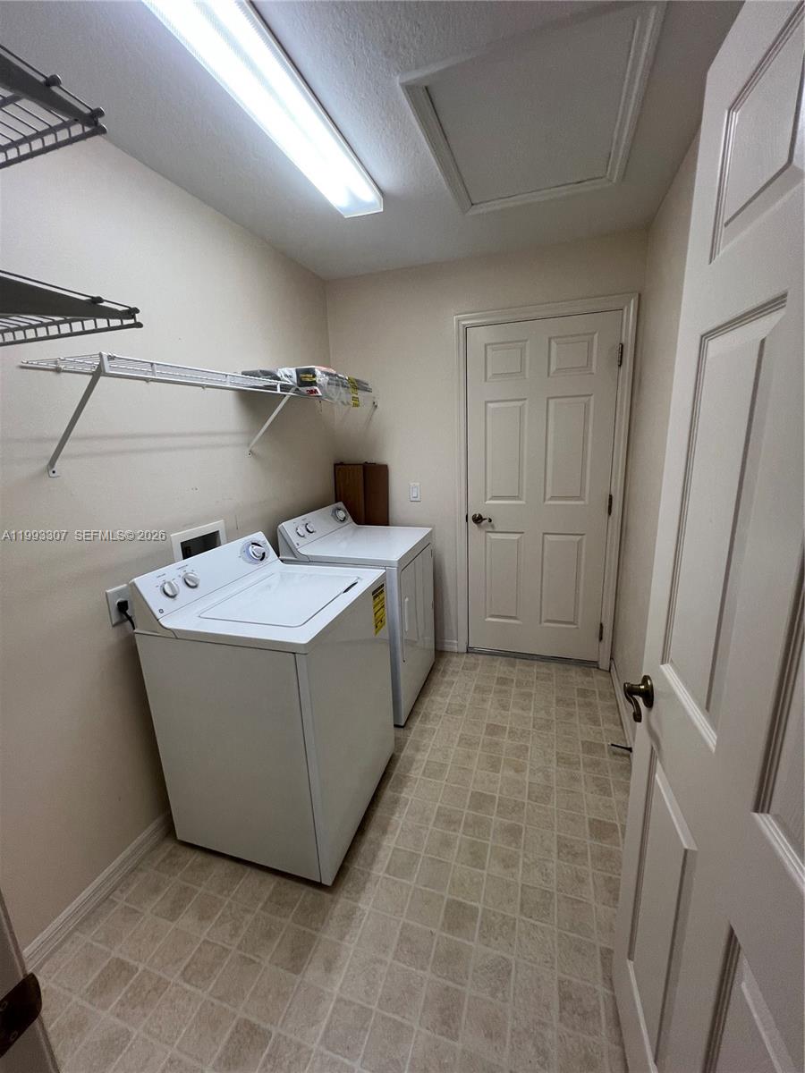 A laundry room features a white washer and dryer, wire shelving, and tile flooring — 1679 SW 156th Ln, Ocala FL 34473, OCALA, FL