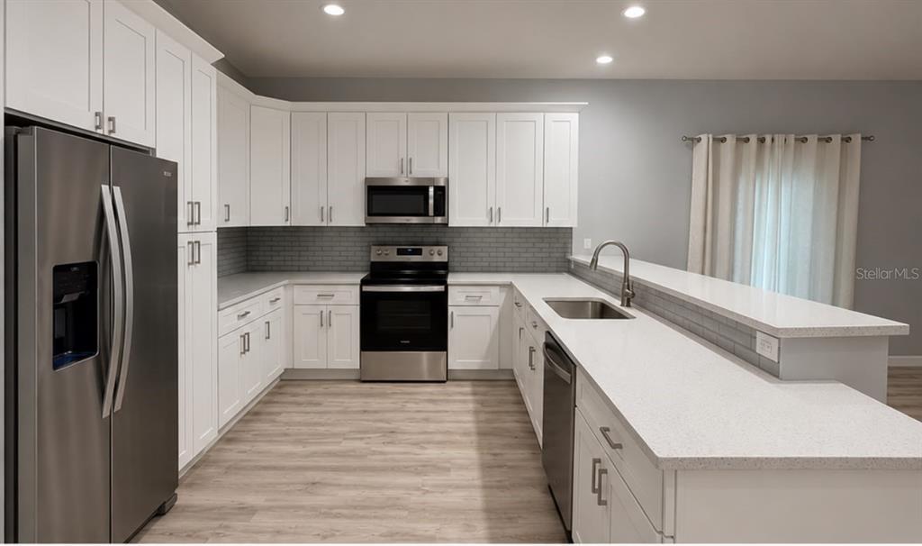 A kitchen features white cabinetry, stainless steel appliances, quartz countertops, and a gray subway tile backsplash — 617 HOLMES AVENUE, DAYTONA BEACH, FL