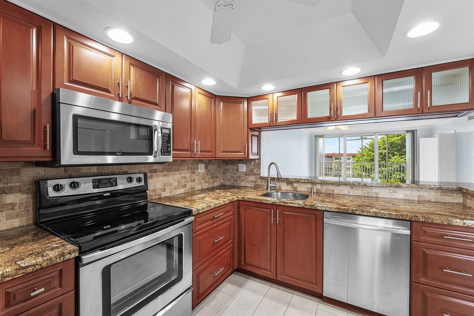 A kitchen with cherry wood cabinets, granite countertops, stainless steel appliances, and a pass-through window — 3150 NE 48th Court # 411, Lighthouse Point FL 33064, LIGHTHOUSE POINT, FL