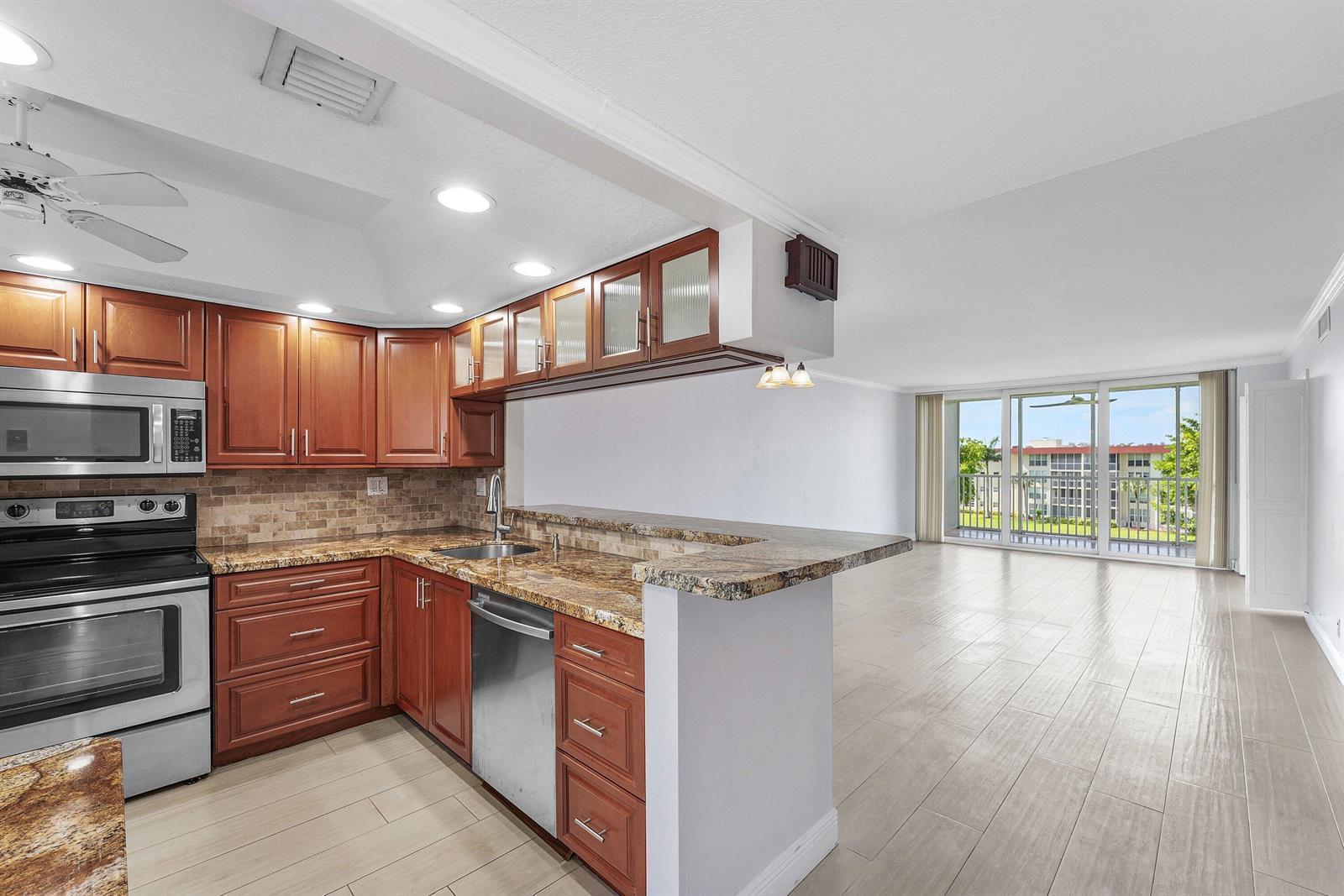 A kitchen with wood cabinets and granite countertops opens to a living area with balcony access — 3150 NE 48th Court # 411, Lighthouse Point FL 33064, LIGHTHOUSE POINT, FL