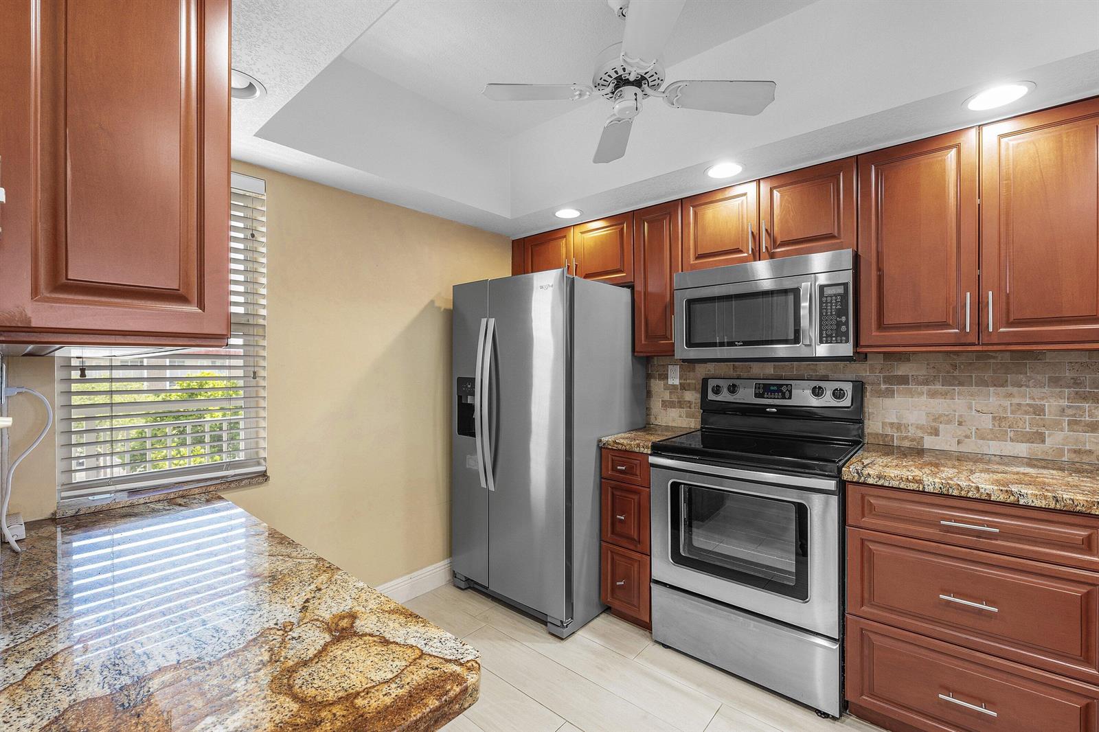 A kitchen featuring wood cabinets, granite countertops, stainless steel appliances, and a ceiling fan — 3150 NE 48th Court # 411, Lighthouse Point FL 33064, LIGHTHOUSE POINT, FL