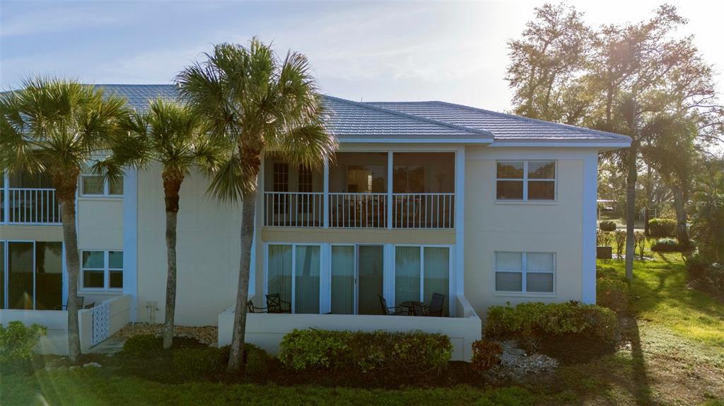 A two-story building with a screened balcony, sliding glass doors, and palm trees in front — 425 CERROMAR TERRACE UNIT 459, VENICE, FL