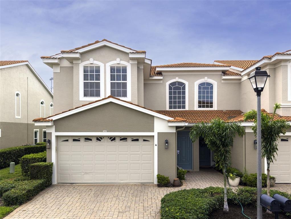 A two-story townhouse with a beige stucco exterior, a tiled roof, and a paved driveway — 1460 RIBOLLA DRIVE, PALM HARBOR, FL