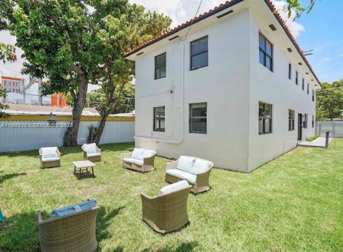 A two-story white building with a grassy backyard featuring outdoor wicker furniture and trees — 584 NW 30th St, Miami FL 33127, MIAMI, FL