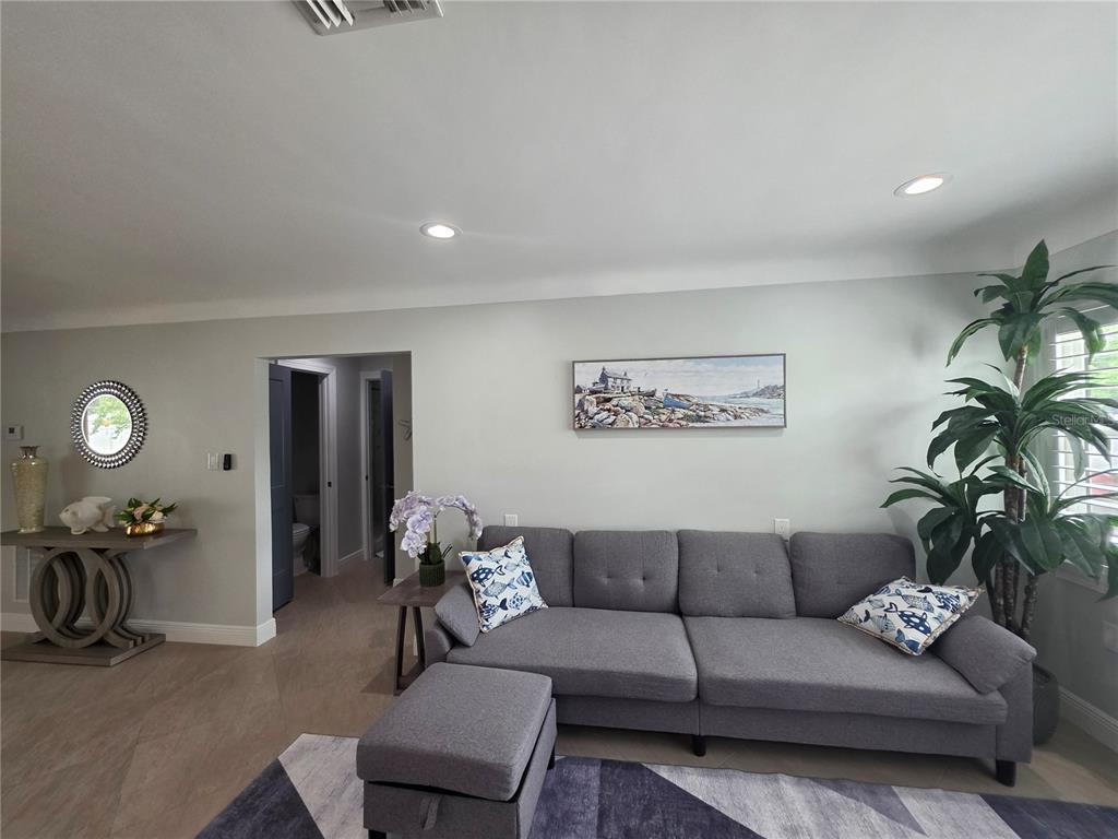 A living room features a gray sofa, a matching ottoman, and a coastal-themed wall painting — 3435 OVERLOOK DRIVE NE, ST PETERSBURG, FL