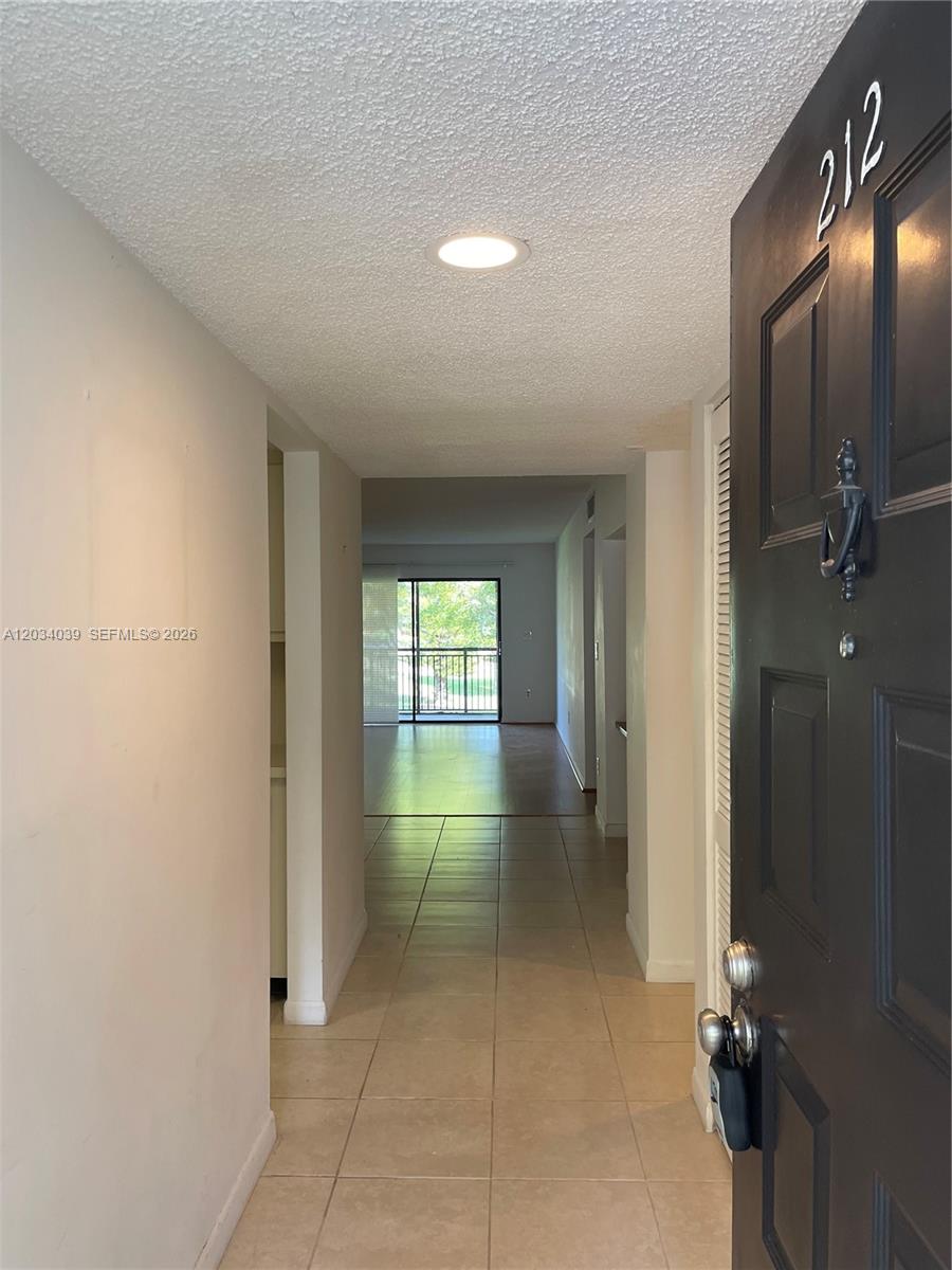 A view from an open front door into a tiled hallway leading to a balcony — 16171 Blatt Blvd # 212, Weston FL 33326, WESTON, FL